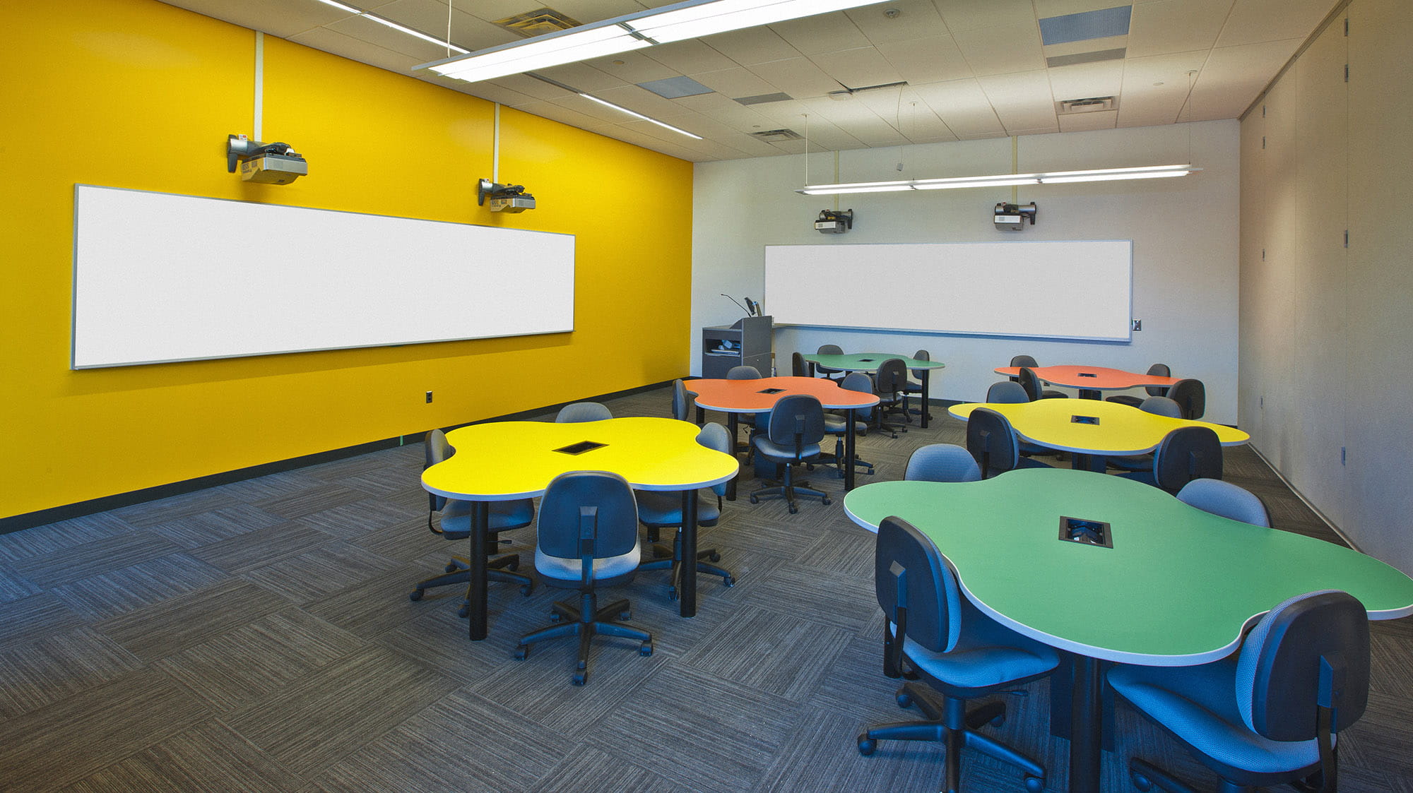 一间黄色墙壁的教室，摆满了五颜六色的变形虫形状的桌子。