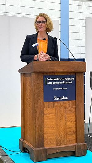 珍妮特·莫里森站在写着“国际学生体验峰会”的讲台后面