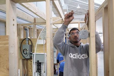 在谢里丹电气实验室，一名学生正在把电线穿过一堵有框的墙