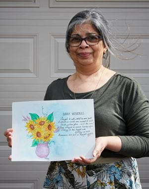一位年长的妇女拿着她创作的一幅题为《阳光的回忆》的画，画中有一束花