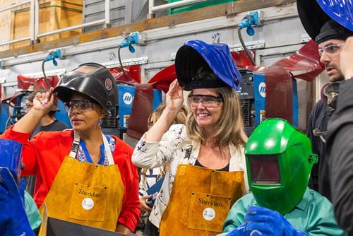 安大略妇女社会经济机会部副部长Charmaine Williams和高等院校部长Jill Dunlop在谢里丹焊接实验室的演示中举起他们的焊接口罩